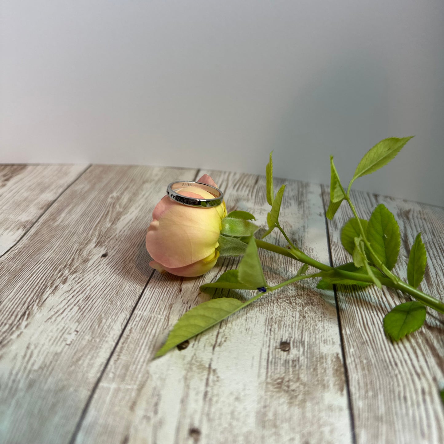 Decorative rose with a ring on top and green leaves on a wooden surface