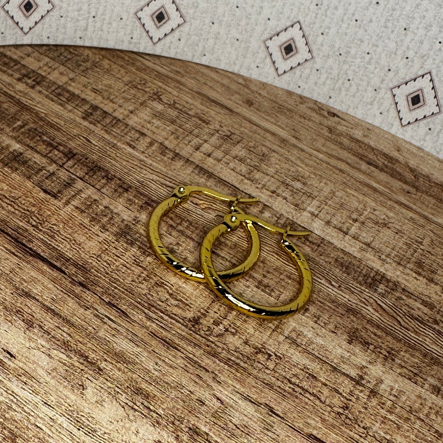 Gold hoop earrings on a wooden surface with a patterned fabric background