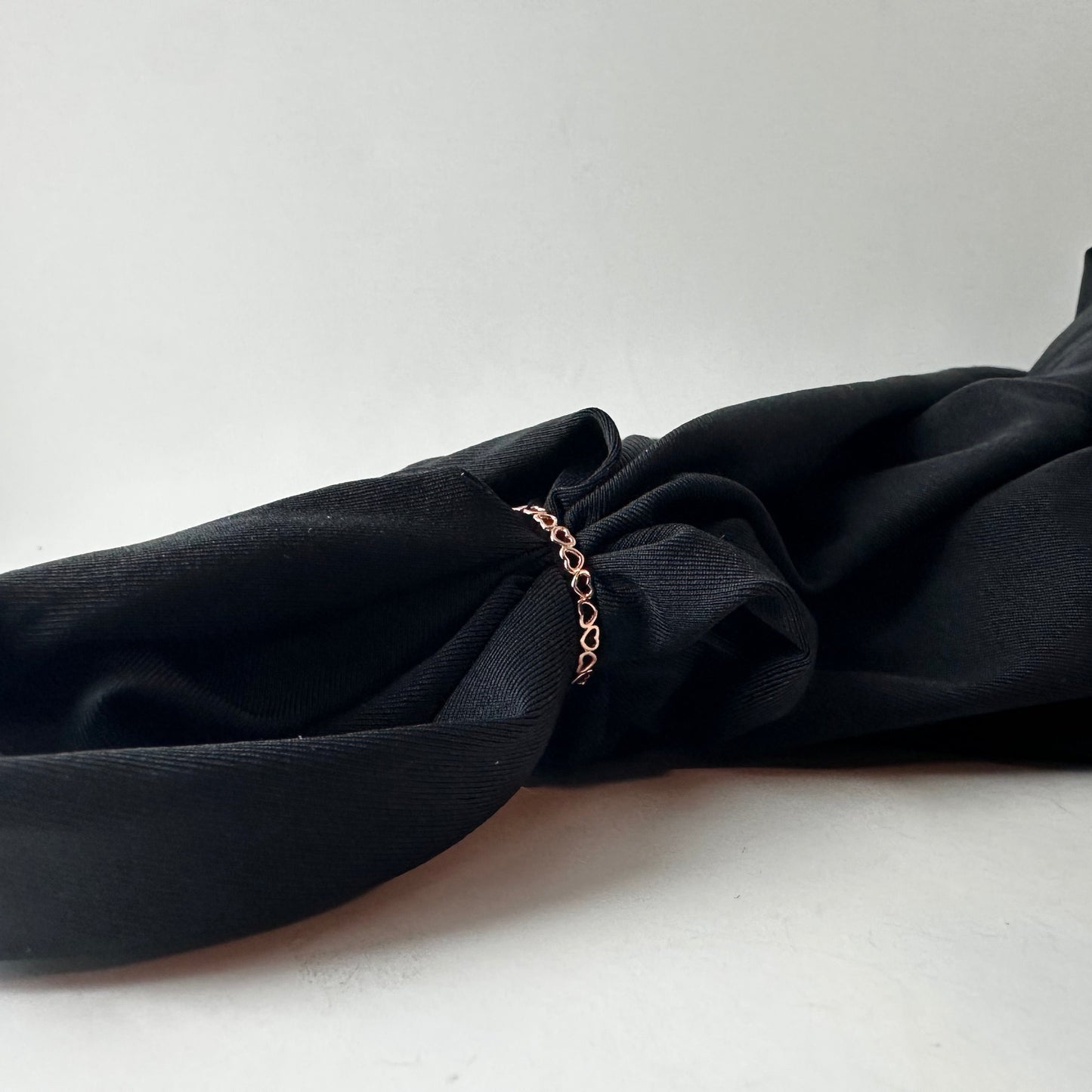Black fabric with a rose gold heart ring on a white background