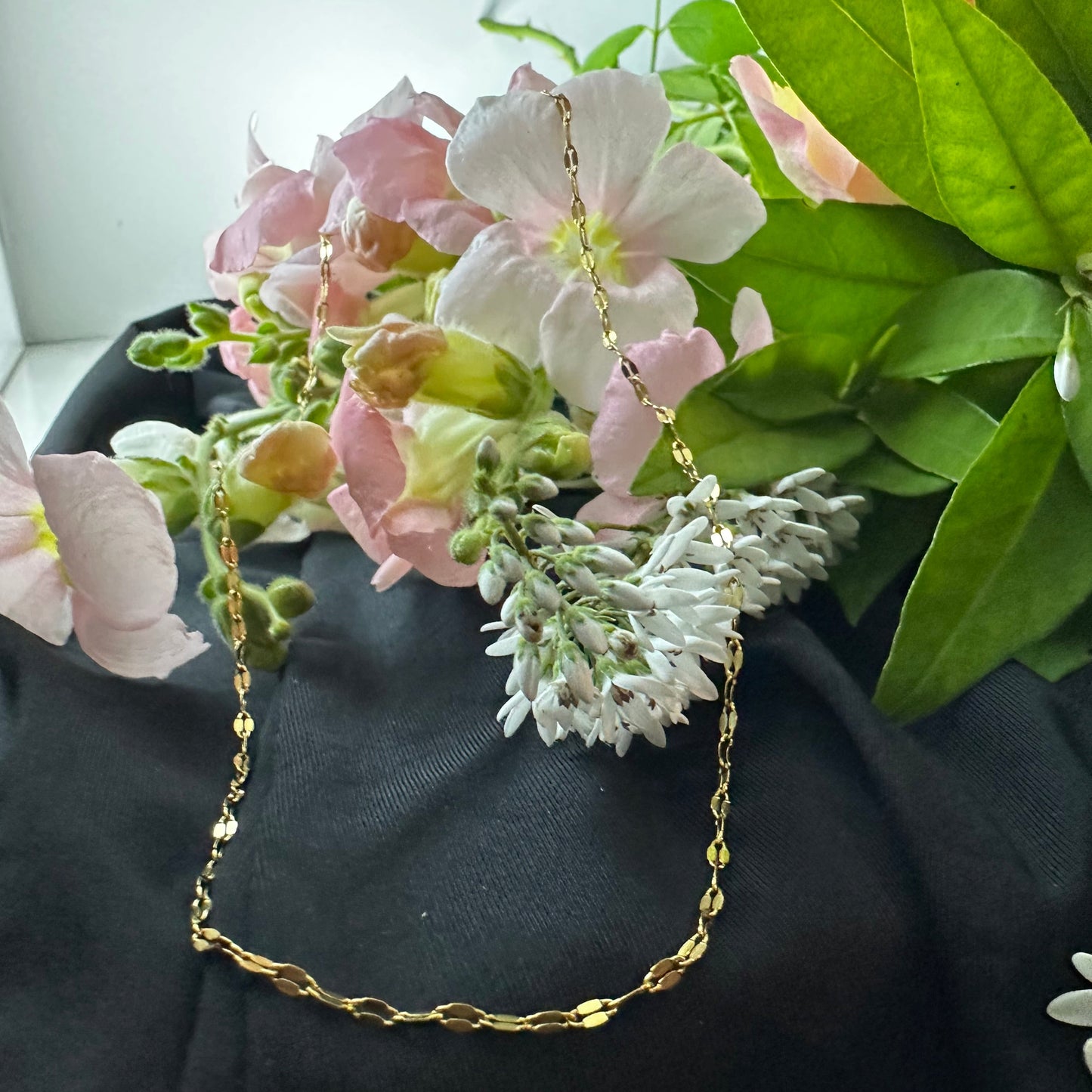 Gold chain necklace draped over a bouquet of flowers with green leaves.