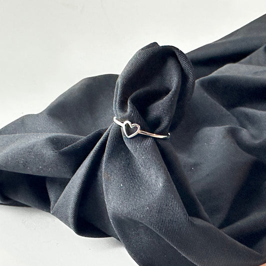 Silver ring with a heart design on a piece of dark gray fabric.