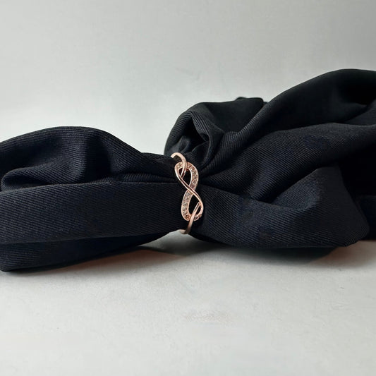 Black fabric with a rose gold infinity symbol ring on a light gray background