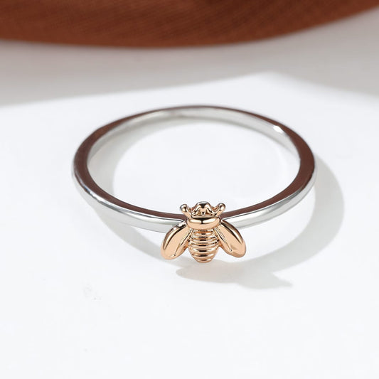 Silver ring with a rose gold bee charm on a white background