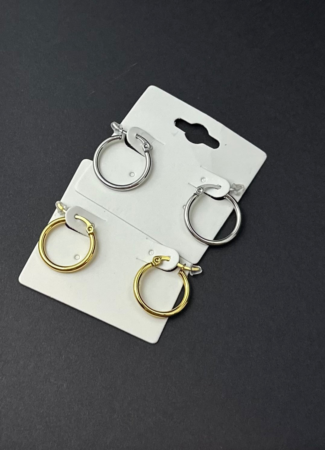 Set of gold and silver hoop earrings on a white card against a black background