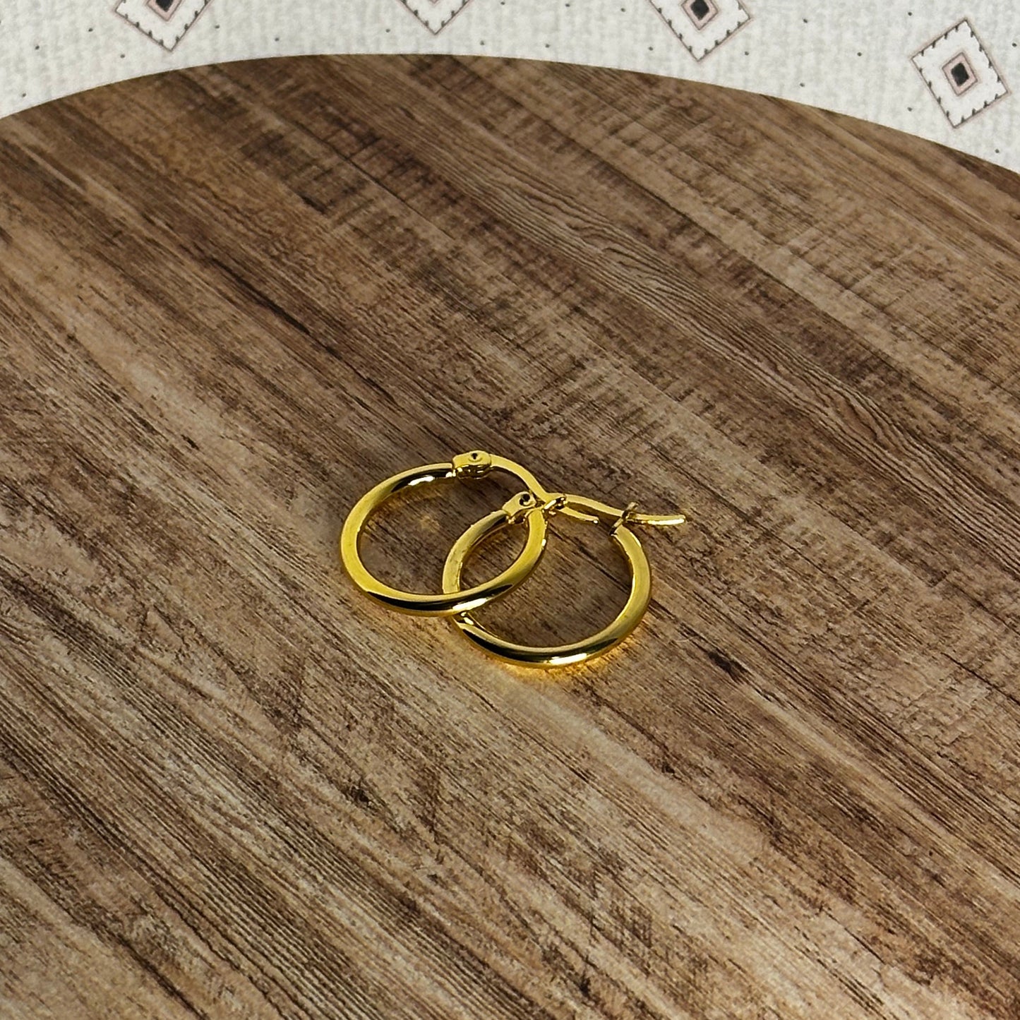 Gold hoop earrings on a wooden surface with a patterned background