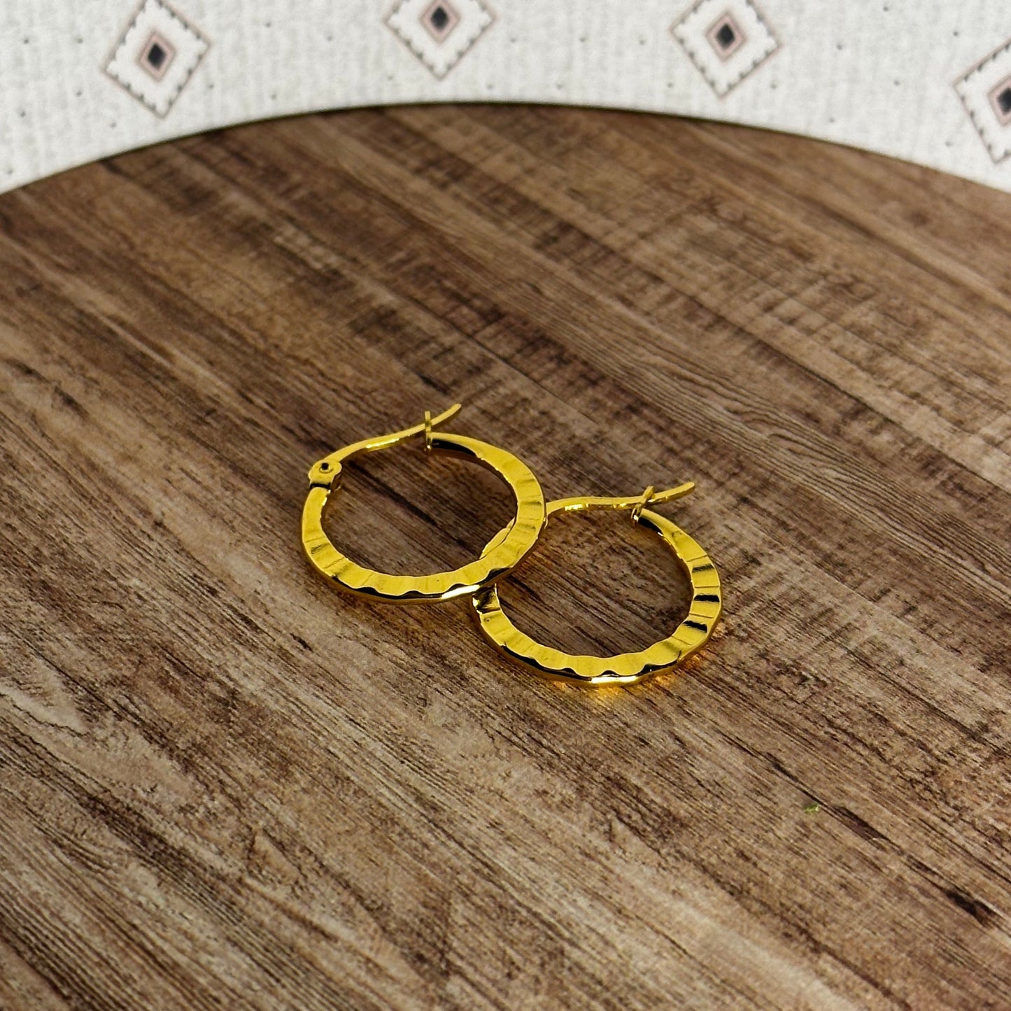Gold hoop earrings on a wooden surface with a patterned fabric background