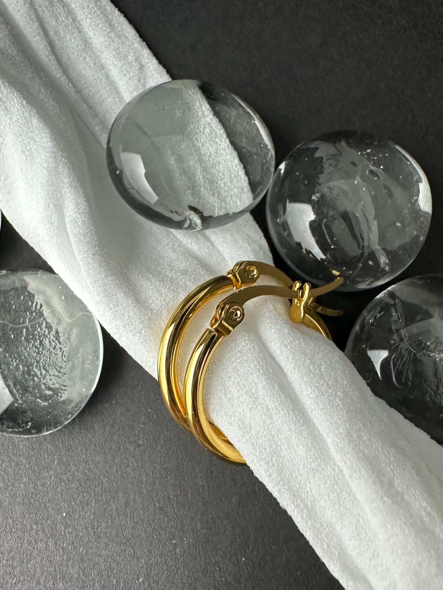 Gold earrings on a white cloth with clear glass balls in the background