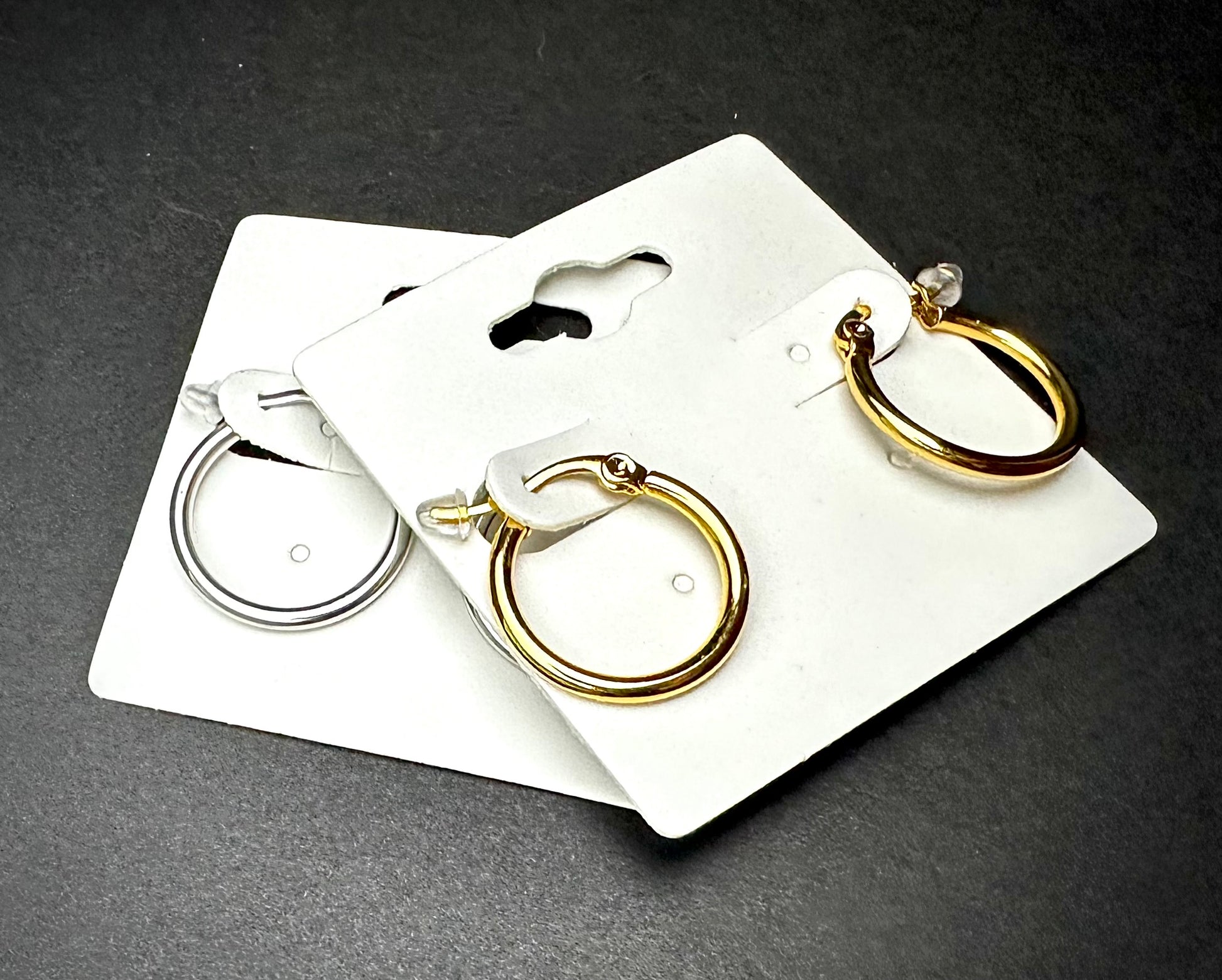 2 pairs of hoop earrings on white cards against a dark background