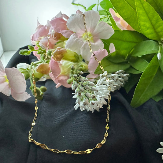 Gold chain necklace draped over a bouquet of flowers with green leaves.