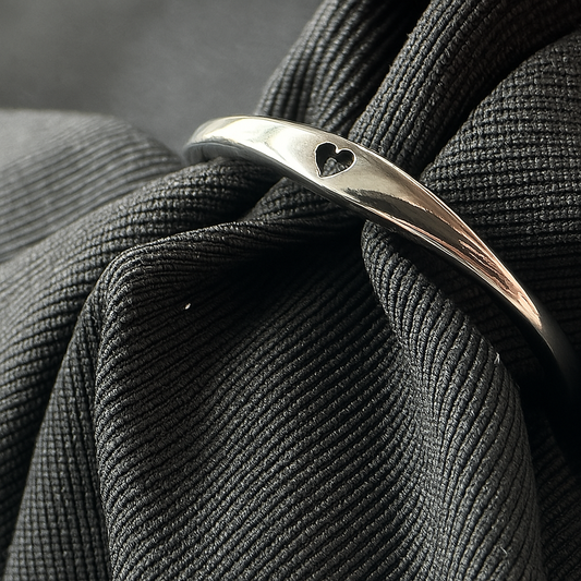 Silver ring with a black enamel heart on a textured black fabric background
