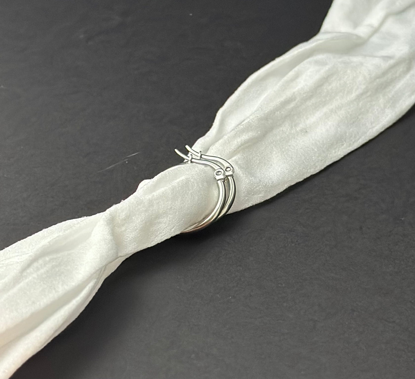 Silver earrings on a white fabric strip against a dark background