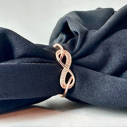 Rose gold infinity ring on a dark blue fabric background